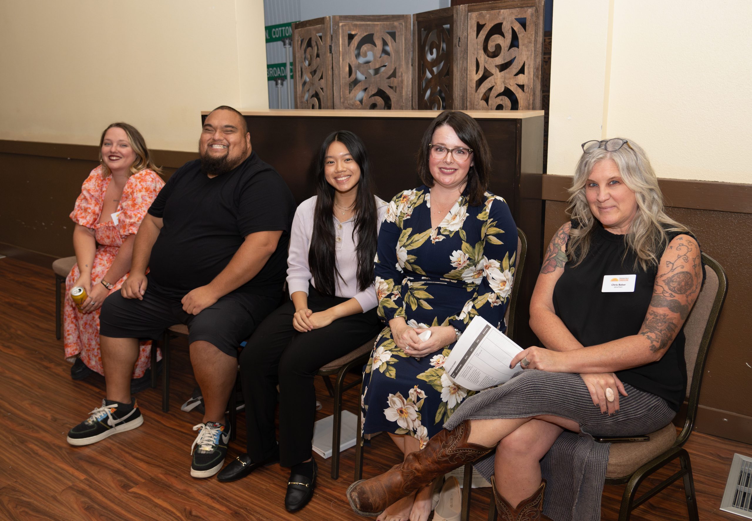 Five smiling people sit on chairs looking at the camera